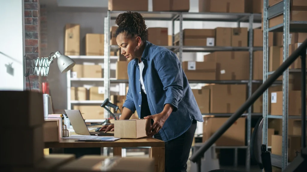 Woman reviewing software in a warehouse while preparing packages