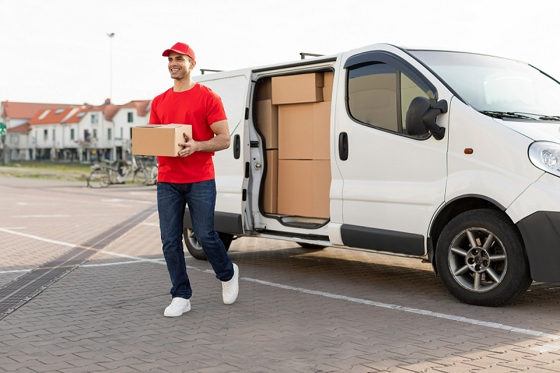 Smiling delivery driver carrying packages from a delivery van