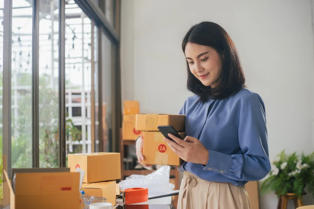 Person preparing packages for shipment while looking at a smartphone